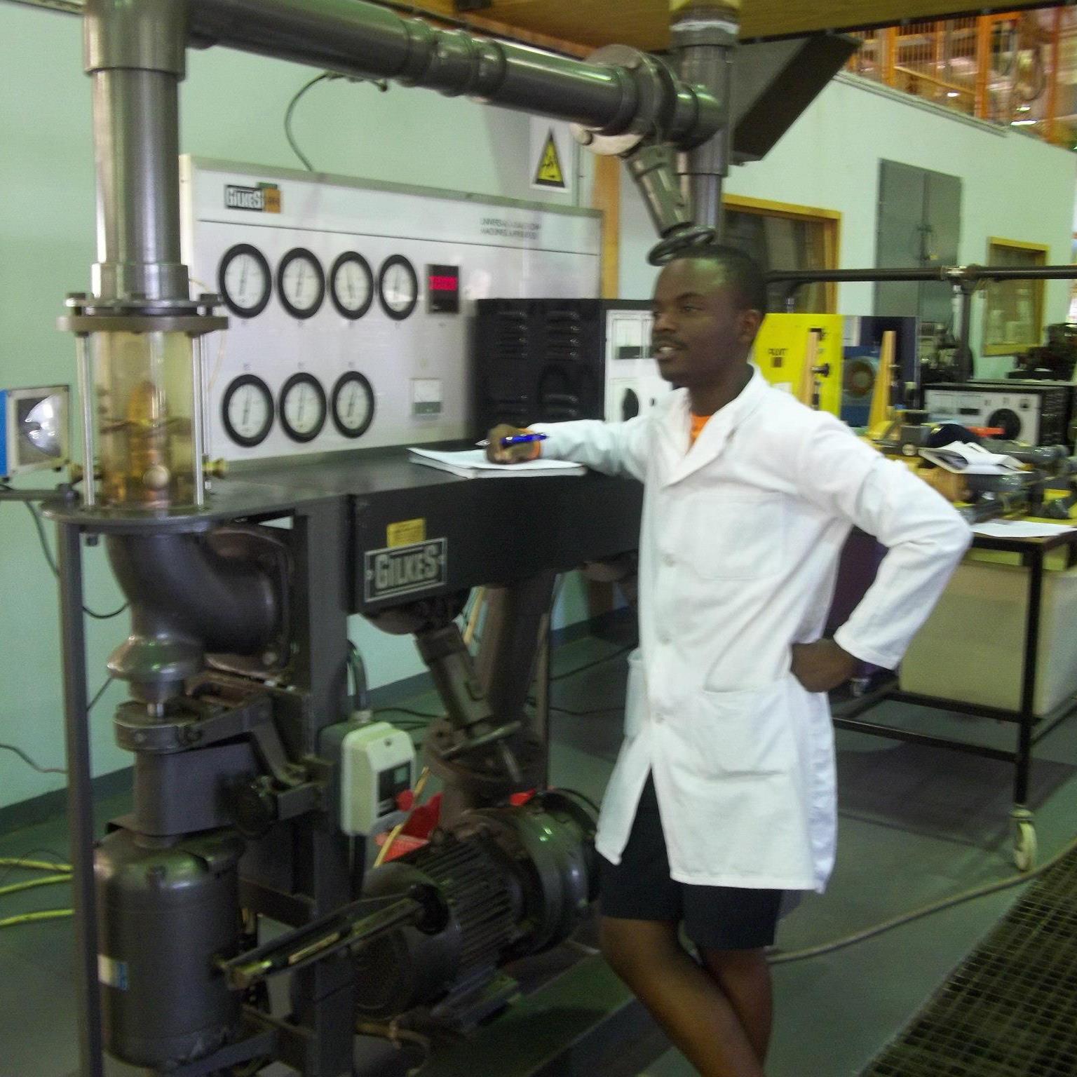 Engineer in a lab coat beside industrial piping and pump equipment during a plant consultancy.