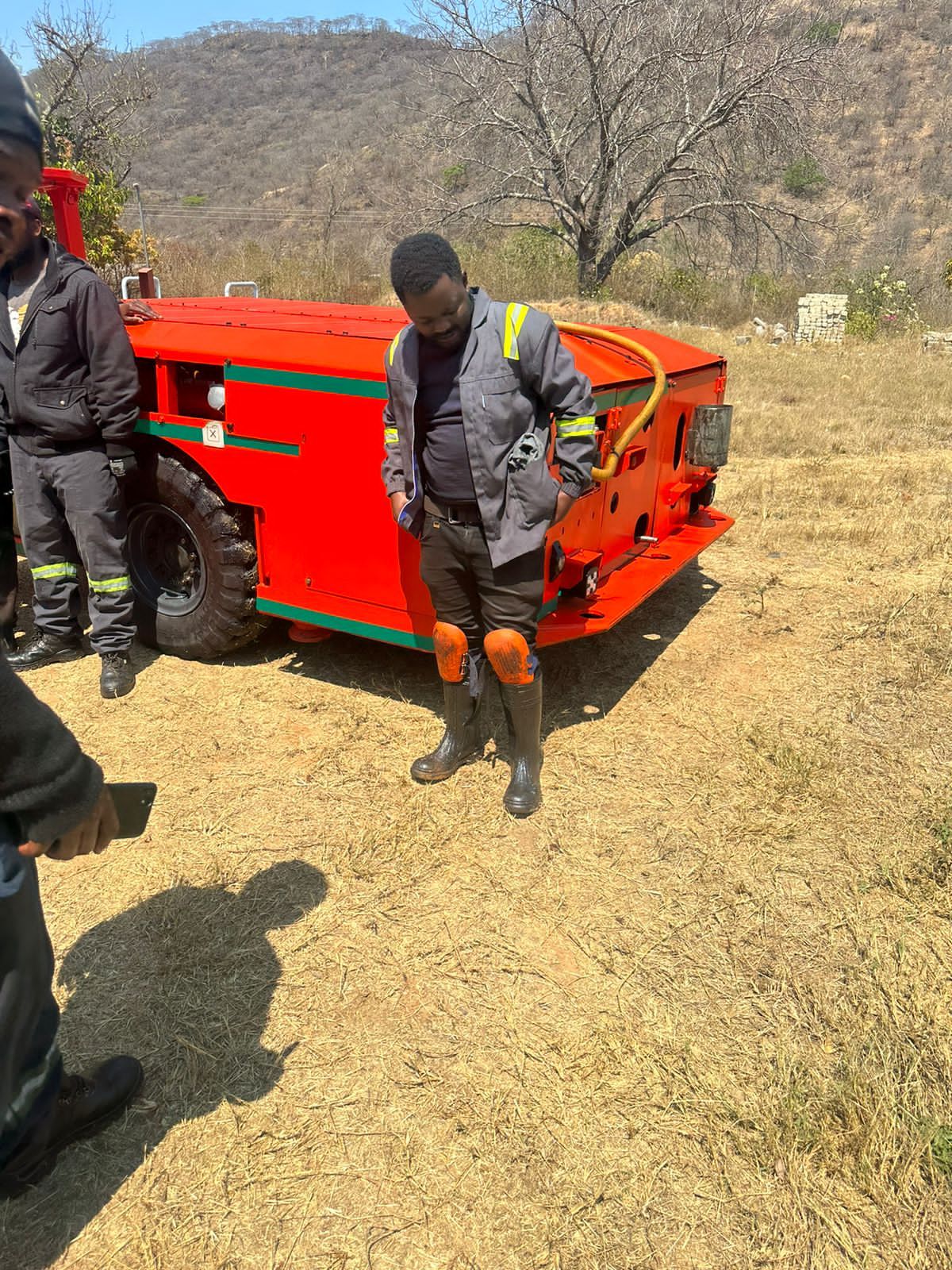 Worker in orange safety gear operating an orange industrial crusher machine outdoors.