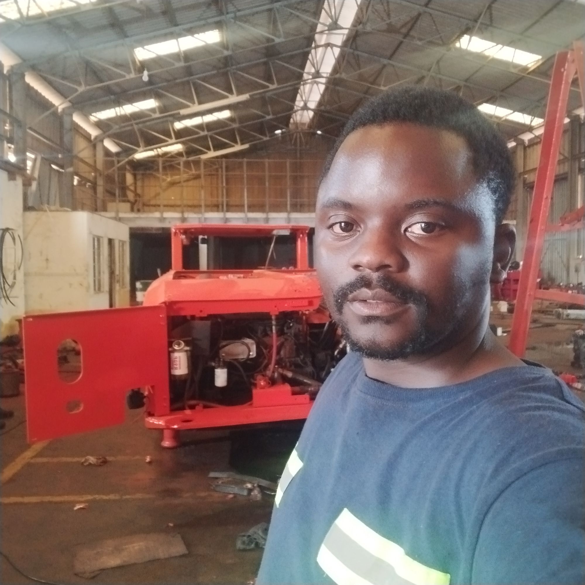 Engineer indoors beside a red industrial support vehicle at a workshop.