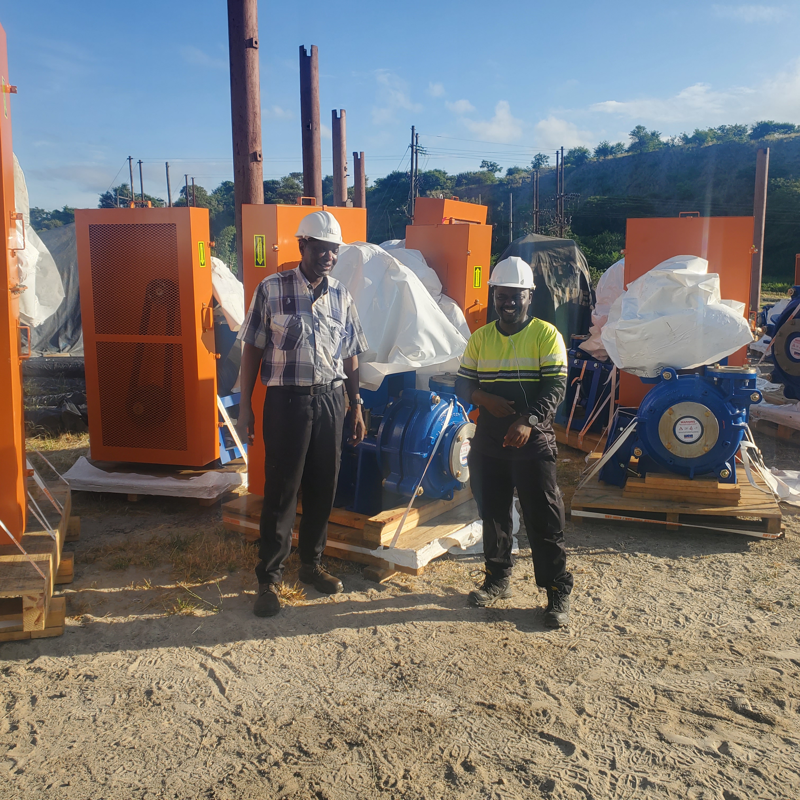 Workers in safety gear beside an orange industrial storage tank on-site.