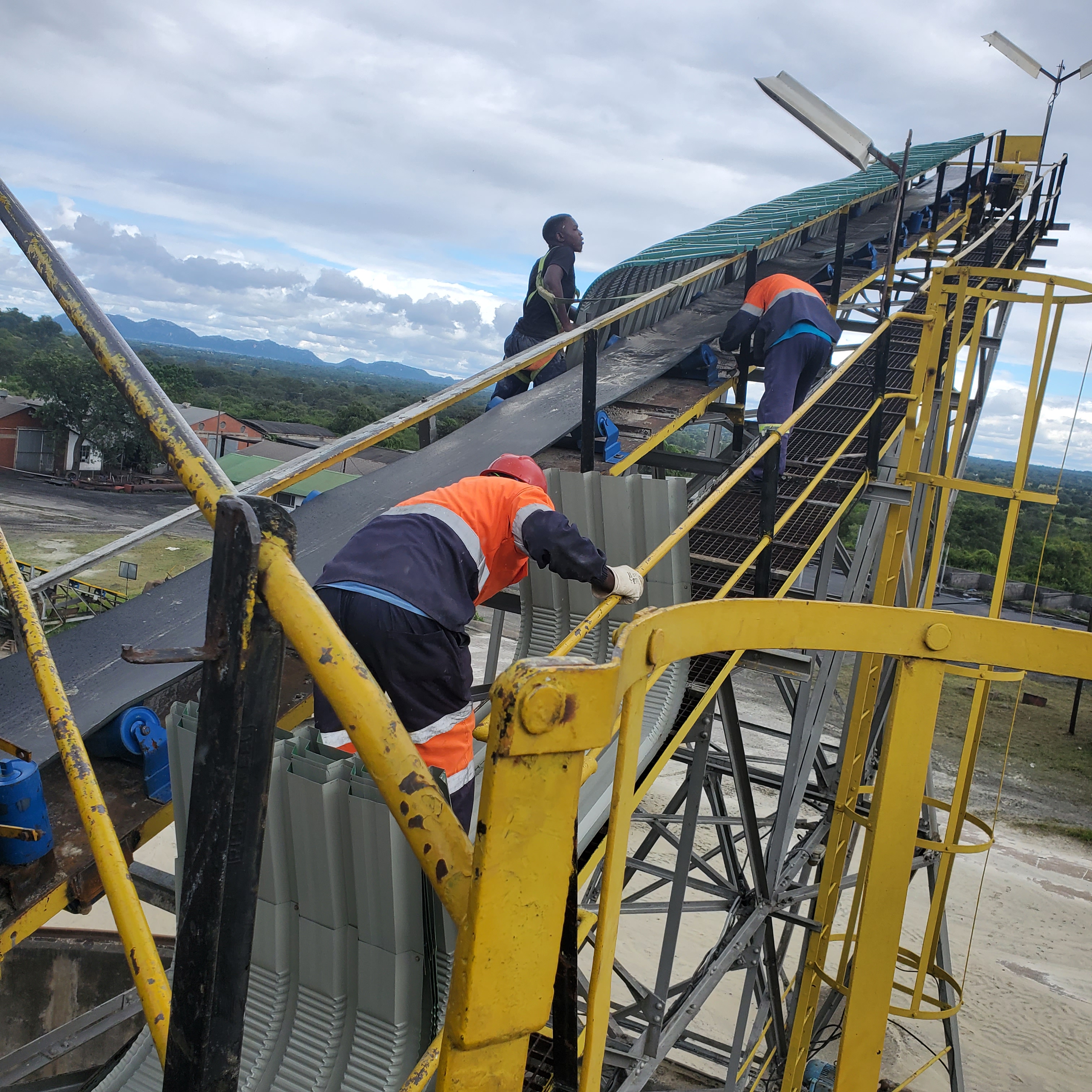 Worker on an elevated yellow conveyor structure at an industrial site.